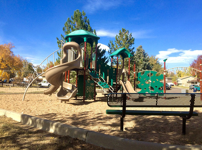 A park situated inside a neighborhood with slides and climbing apparatuses, swing and a park bench