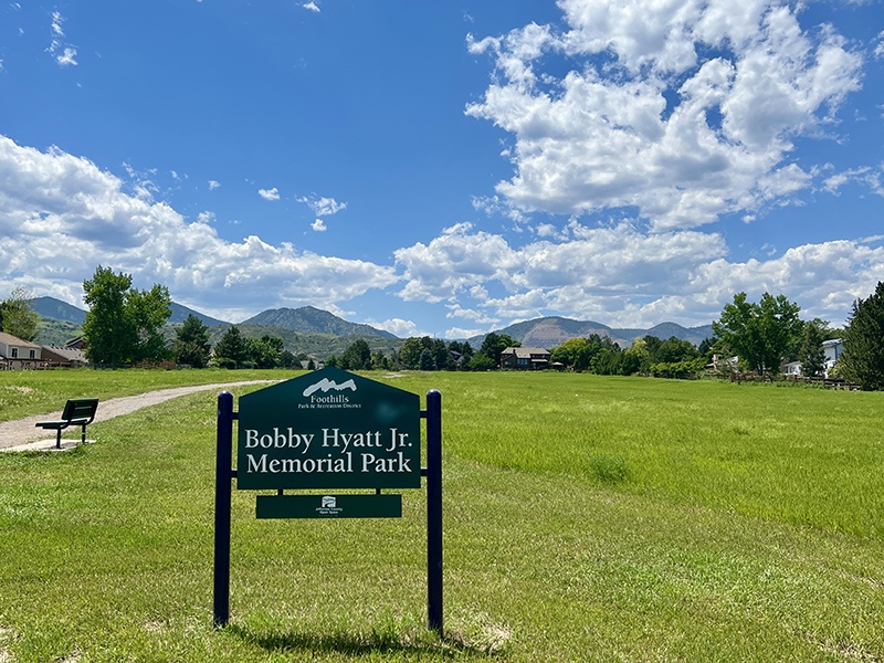 Green grass park, a crusher fines trail and bench with a park sign reading Bobby Hyatt Jr. Memorial Park