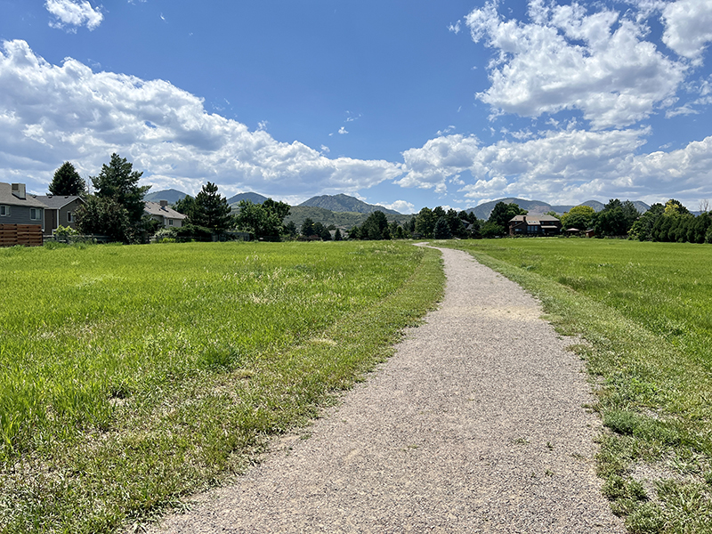 A crusher fines trail with grass on both sides of the trail with views of the foothills