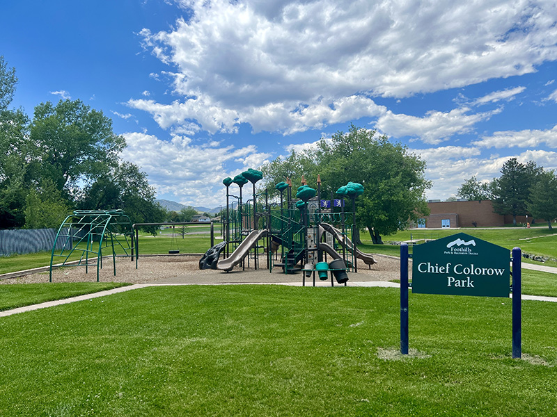 A playground with slides, climbing apparatuses, and a tire swing with the park sign reading Chief Colorado Park