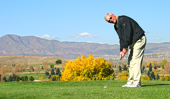 Golfer setting up to chip the ball with mountains in the background.