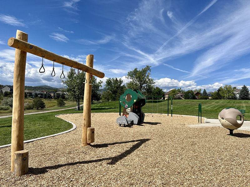 A playground with climbing apparatuses and swings with green grass in the background