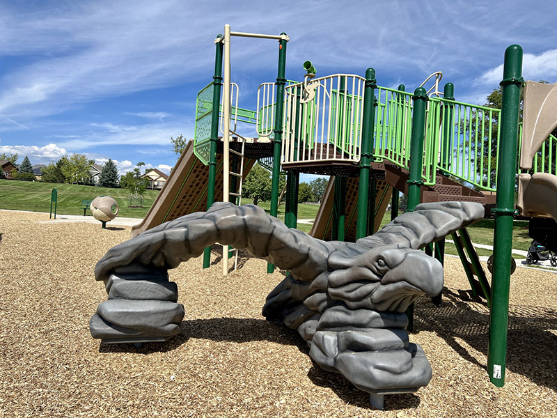 A playground with two slides, climbing apparatuses, and an eagle shaped climber with green grass in the background