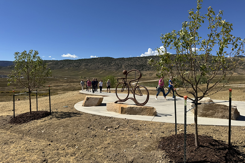 Metal art installation of a biker off the Dutch Creek Trail with people walking in the background.