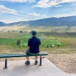 A man sitting on a bench off the Dutch Creek Trail overlooking the Meadows Golf Club and foothills in the background.