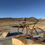 Iron sculpture of a person on a bicycle mounted on a large rock near the Dutch Creek Trail.