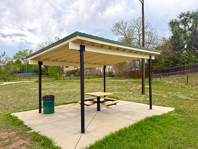 A small park shelter with a table and bench seats in a greenbelt.