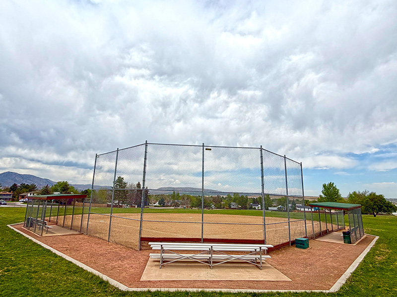 An empty baseball field surrounded by grass with a mountain backdrop.